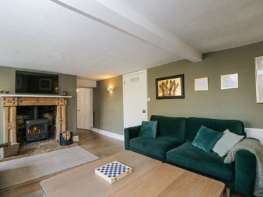 A living room with a green sofa wooden coffee table a fireplace with a fire and wall art at The Old School House in Lower Swell near Stow-On-The-Wold