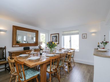 A dining room with a wooden table set for eight with plates glasses and a flower vase at The Old School House in Lower Swell near Stow-On-The-Wold