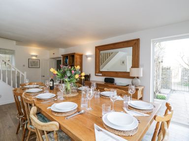 A dining room with a wooden table set with plates glasses and cutlery a flower vase on the table and a large mirror on the wall at The Old School House in Lower Swell near Stow-On-The-Wold