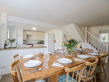A dining area with a wooden table set with plates, glasses, and cutlery near a kitchen and staircase at The Old School House in Lower Swell near Stow-On-The-Wold