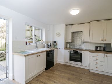 A kitchen with white cabinets wooden countertops a black dishwasher an oven a window and a door at The Old School House in Lower Swell near Stow-On-The-Wold