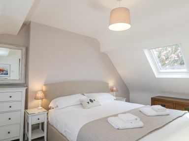 A bedroom with a bed white bedding towels bedside tables lamps mirror dresser and a skylight window at The Old School House in Lower Swell near Stow-On-The-Wold