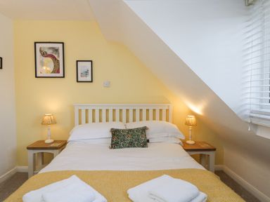 A bedroom with a double bed two bedside tables with lamps and framed pictures on the wall at The Old School House in Lower Swell near Stow-On-The-Wold