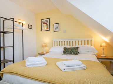 A bedroom with a double bed two bedside tables with lamps and a shelving unit at The Old School House in Lower Swell near Stow-On-The-Wold