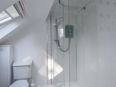 A bathroom with a toilet and a glass-enclosed shower under a sloped ceiling at The Old School House in Lower Swell near Stow-On-The-Wold