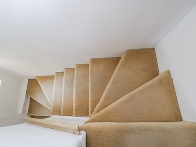A beige carpeted staircase with white walls and a wooden handrail at The Old School House in Lower Swell near Stow-On-The-Wold