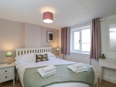 A bedroom with a double bed two bedside tables with lamps and a window with curtains at The Old School House in Lower Swell near Stow-On-The-Wold