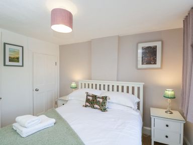 A bedroom with a bed side tables lamps and framed pictures at The Old School House in Lower Swell near Stow-On-The-Wold