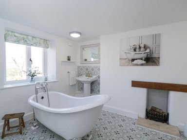A bathroom with a freestanding bathtub a sink a small wooden stool and a fireplace at The Old School House in Lower Swell near Stow-On-The-Wold