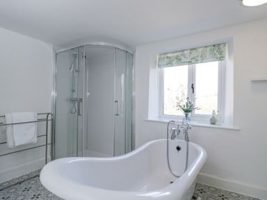 A bathroom with a freestanding bathtub shower enclosure towel rack and window at The Old School House in Lower Swell near Stow-On-The-Wold
