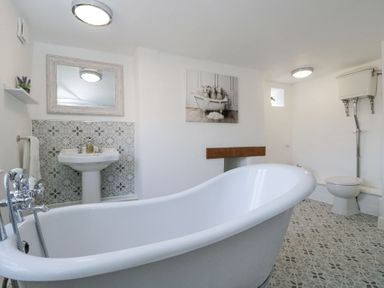 A bathroom with a freestanding bathtub a pedestal sink a toilet and patterned floor tiles at The Old School House in Lower Swell near Stow-On-The-Wold