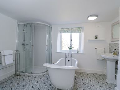 A bathroom with a freestanding bathtub shower enclosure sink and window at The Old School House in Lower Swell near Stow-On-The-Wold