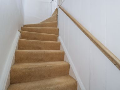 A staircase with beige carpet and a wooden handrail on the right wall at The Old School House in Lower Swell near Stow-On-The-Wold