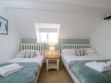 A bedroom with two single beds a nightstand with a lamp and a window at The Old School House in Lower Swell near Stow-On-The-Wold