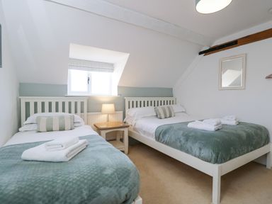 A bedroom with two beds a bedside table with a lamp and a window at The Old School House in Lower Swell near Stow-On-The-Wold