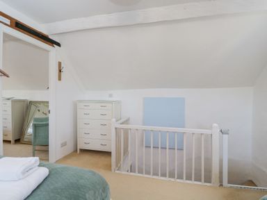 An attic bedroom area with a white chest of drawers a staircase with a white railing and a blue square on the wall at The Old School House in Lower Swell near Stow-On-The-Wold
