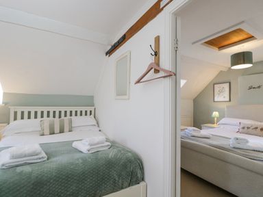 Two adjacent bedrooms each with a bed, bedside table, lamp, and neatly folded towels at The Old School House in Lower Swell near Stow-On-The-Wold