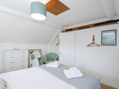 A bedroom with a bed with towels folded on it a white dresser a green chair a mirror and a door at The Old School House in Lower Swell near Stow-On-The-Wold