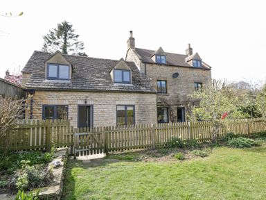 Stone house with wooden fence and garden with grass and plants at The Old School House in Lower Swell near Stow-On-The-Wold