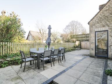 An outdoor patio with a dining table and chairs and an umbrella next to a stone building at The Old School House in Lower Swell near Stow-On-The-Wold