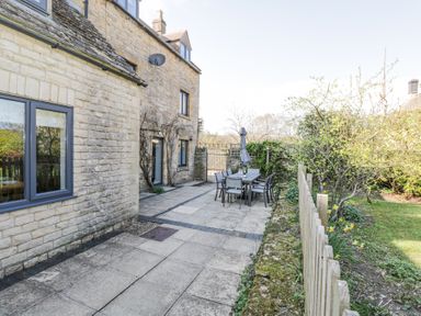 An outdoor patio with a table and chairs with an umbrella next to a stone house and garden at The Old School House in Lower Swell near Stow-On-The-Wold