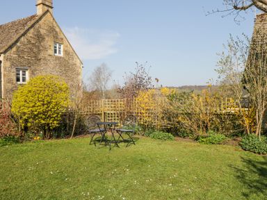 A garden with a small table and two chairs in front of a stone house at The Old School House in Lower Swell near Stow-On-The-Wold