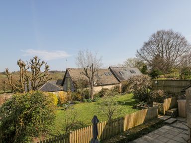 A fenced garden with trees shrubs and a house in the background at The Old School House in Lower Swell near Stow-On-The-Wold