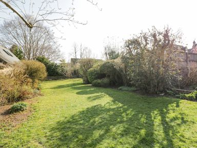 A garden with grass lawn surrounded by various bushes and trees at The Old School House in Lower Swell near Stow-On-The-Wold