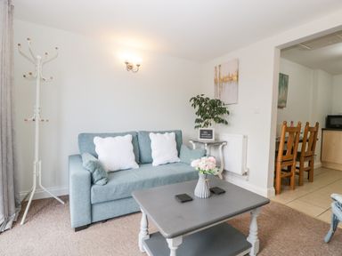 A living room with a blue sofa white pillows coffee table with flowers and a plant at Thornhills Cottage in Othery near Middlezoy