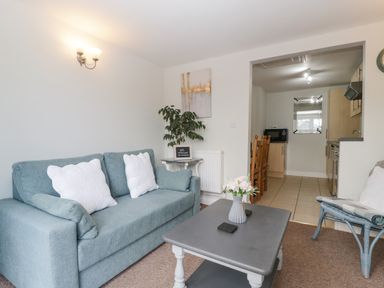A living room with a blue sofa white pillows coffee table with flowers and a view into a kitchen and dining area at Thornhills Cottage in Othery near Middlezoy