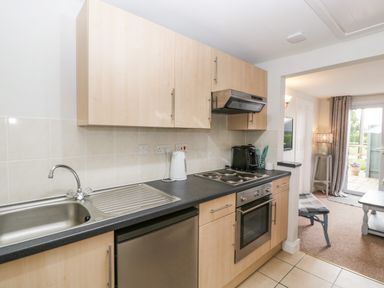 A kitchen with a sink stove oven and cabinets next to a living room with a lamp and window doors at Thornhills Cottage Othery near Middlezoy