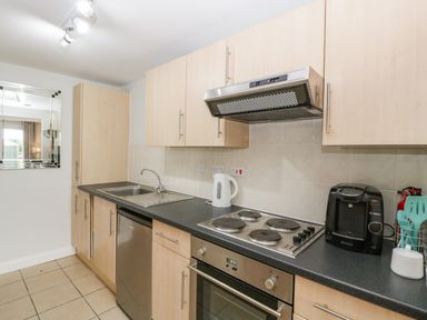 A kitchen with light wood cabinets a black countertop electric stove stainless steel oven dishwasher kettle coffee machine and sink at Thornhills Cottage in Othery near Middlezoy
