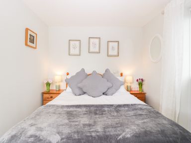 A bedroom with a double bed gray pillows and blanket wooden nightstands with lamps and flowers at Thornhills Cottage in Othery near Middlezoy
