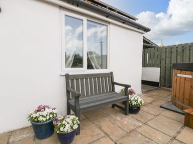 An outdoor patio area with a wooden bench and flower pots near a white exterior wall at Thornhills Cottage in Othery near Middlezoy