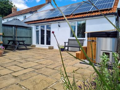 A patio with a wooden bench hot tub picnic table and solar panels on the roof at Thornhills Cottage in Othery near Middlezoy