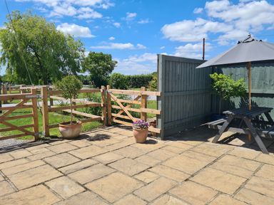 A patio with potted plants wooden fence and a picnic table with umbrella at Thornhills Cottage Othery near Middlezoy