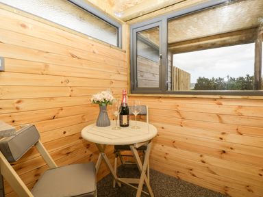 A small corner with wooden walls with a table holding a vase with flowers a bottle and two wine glasses and two chairs at Thornhills Lodge in Othery near Middlezoy