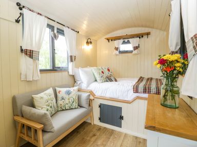 A small bedroom with a bed, sofa, windows with curtains, and a vase of flowers on a wooden surface at Thornhills Lodge in Othery near Middlezoy