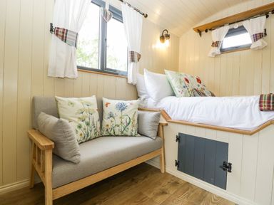 A small room with a grey sofa with floral cushions and a raised bed with white pillows and floral cushions at Thornhills Lodge in Othery near Middlezoy