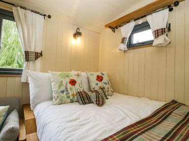 A bedroom with a bed decorated with floral and plaid pillows and white curtains on windows at Thornhills Lodge Othery near Middlezoy