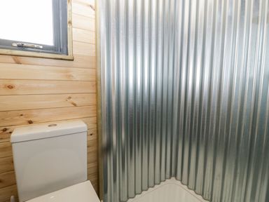 A bathroom with a toilet next to a corrugated metal shower enclosure and a wooden wall near a window at Thornhills Lodge in Othery near Middlezoy