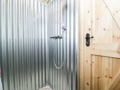 A shower area with corrugated metal walls and a wooden door with black handle at Thornhills Lodge in Othery near Middlezoy