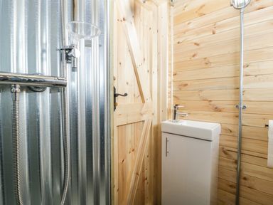 A small bathroom with a sink cabinet and shower area with corrugated metal wall and wooden panel walls at Thornhills Lodge in Othery near Middlezoy