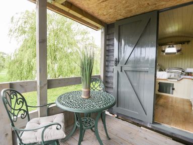 A small outdoor patio with a round metal table and two chairs with cushions next to an open door leading to a room with a bed at Thornhills Lodge in Othery near Middlezoy