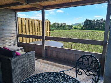 A covered wooden deck with outdoor seating and table overlooking a field at Thornhills Lodge Othery near Middlezoy