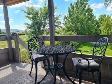 A patio with a metal table and two chairs with cushions overlooking a green garden at Thornhills Lodge in Othery near Middlezoy