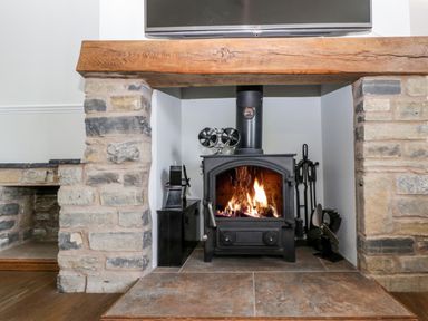 A lit wood stove with fireplace tools and a wooden mantel in a room at Somerset House in Othery near Middlezoy