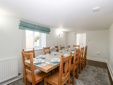 A dining room with a wooden table set for eight people with wooden chairs and flowers on the table at Somerset House in Othery near Middlezoy
