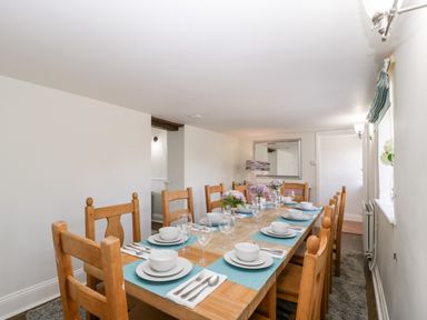 A dining room with a wooden table set for eight with white dishes and blue placemats at Somerset House Othery near Middlezoy