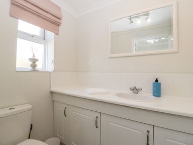 A bathroom with a toilet, a sink with a cabinet, a mirror, a window with a blind, and a bottle of soap at Somerset House in Othery near Middlezoy